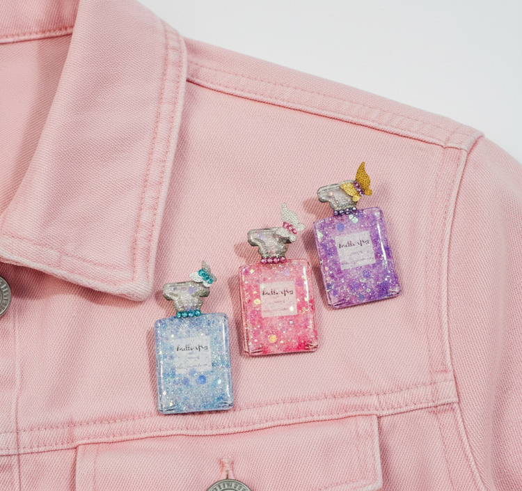 Three colorful perfume bottle pins on a pink jacket
