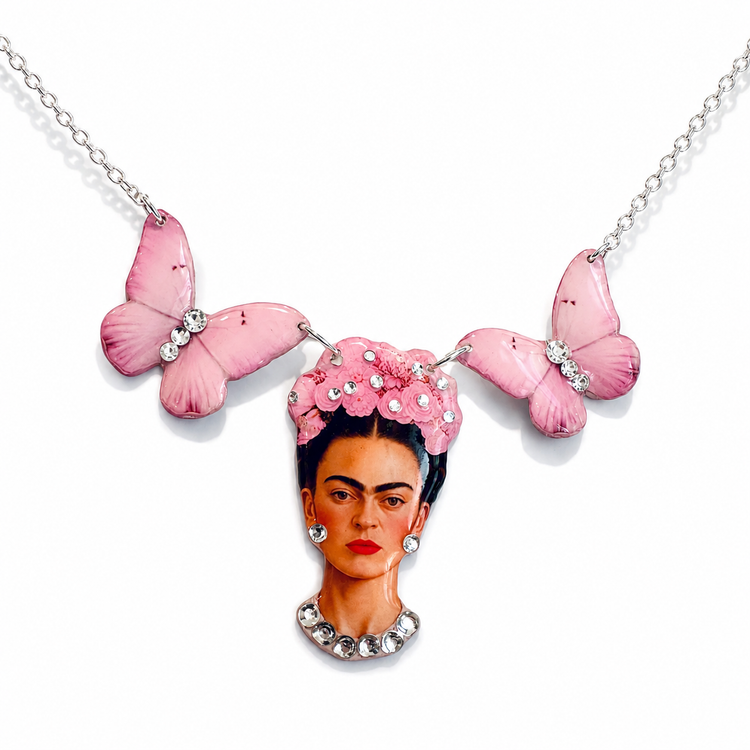 A silver chain necklace featuring a pendant shaped like Frida Kahlo's portrait, with pink enamel butterfly wings on each side and small clear rhinestones, shown on a white background.
