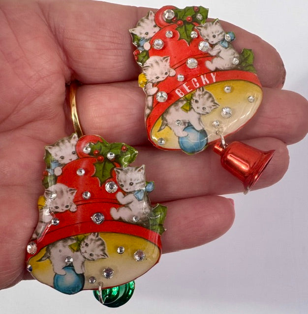 Decorative Christmas brooch with kittens and a bell held in a hand.