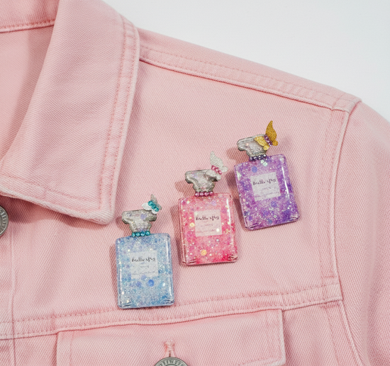 Three colorful perfume bottle pins on a pink jacket