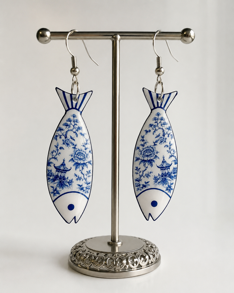 A pair of dangling fish-shaped earrings with a blue and white floral pattern