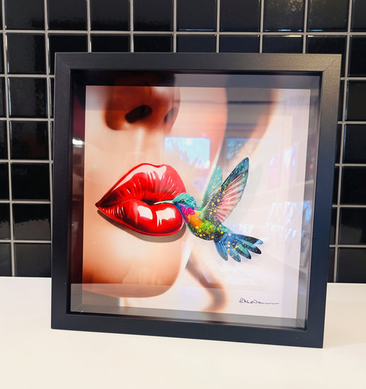 Framed artwork of a woman's face with red lips and a colorful hummingbird.