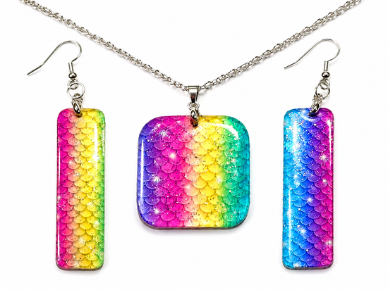A jewelry set featuring a square pendant and two matching rectangular drop earrings with a vibrant rainbow gradient and scale-like texture, suspended from a silver chain on a white background.